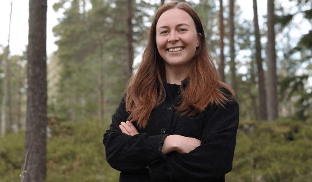 En kvinna som står i en skog med armarna i kors.
